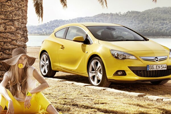 Chica en amarillo y auto Opel Astra GT amarillo en una playa tropical