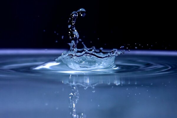 Une goutte tombe dans une flaque d eau sur un fond sombre