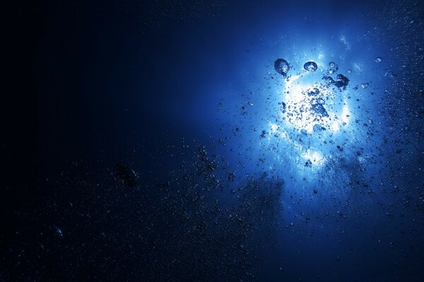 Fotografía submarina del Sol desde debajo de la columna de agua azul con burbujas