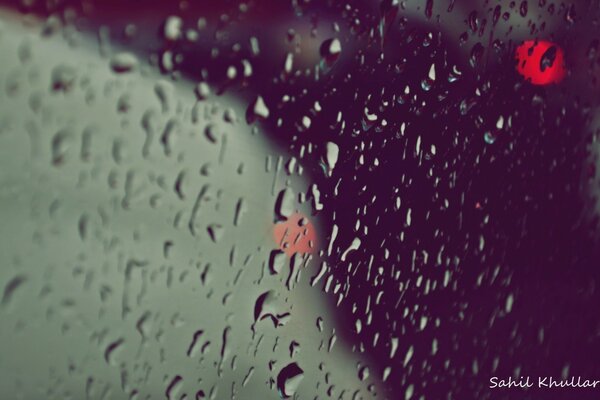 Imagen de gotas de agua en vidrio con luces rojas