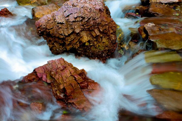 धुंधली पृष्ठभूमि पर झरने के बीच भूरे रंग के पत्थर