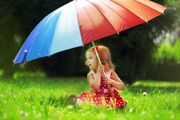 A girl in a polka dot dress sitting on the grass under a huge bright umbrella