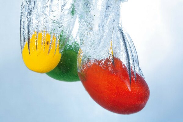 Las frutas amarillas, rojas y verdes brillantes caen al agua