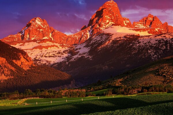 Schneebedeckte Berge mit grüner Wiese bei Sonnenuntergang