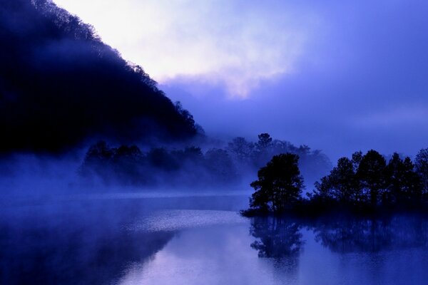 Nebel über dem Teich in der Nähe der Berge in blauen Farbtönen