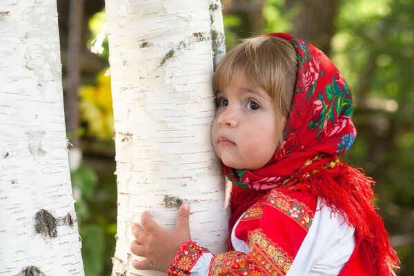 Una niña con un pañuelo rojo abrazando un abedul