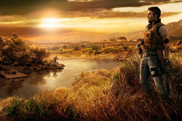 The hero of the game Farcry 4 in full combat gear stands on the high bank of the river knee-deep in the grass against the background of the sunset sky