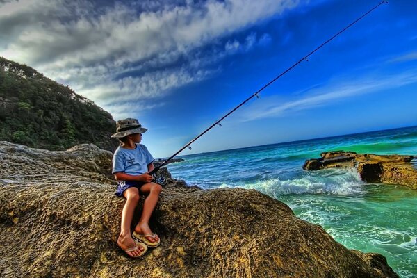 Un niño en Panamá con una caña de pescar se sienta en la orilla de piedra del mar azul durante el día