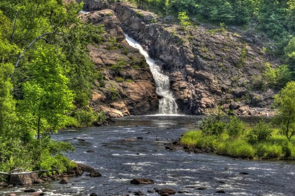 The waterfall flows into a mountain river in the middle of the forest