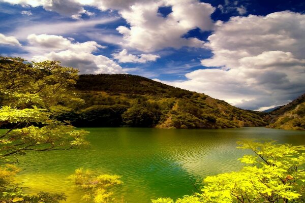 Ein See inmitten grüner Hügel. Blauer Himmel und weiße Wolken