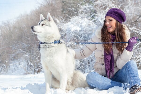 Hermosa chica sentada con Husky en la nieve