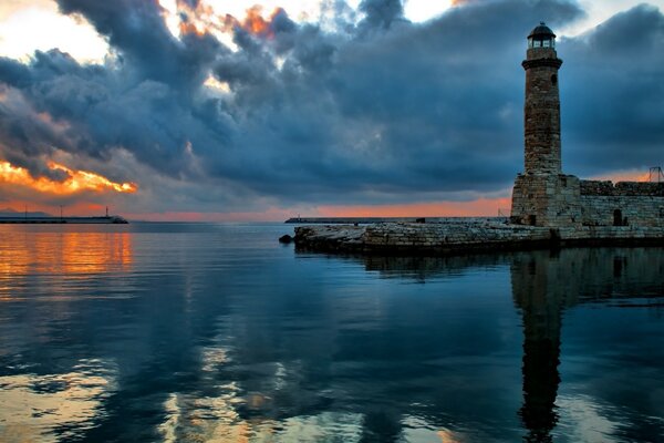 The lighthouse is reflected in the waters of the evening sea