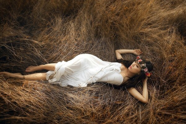 A girl in a white dress is lying on dry grass