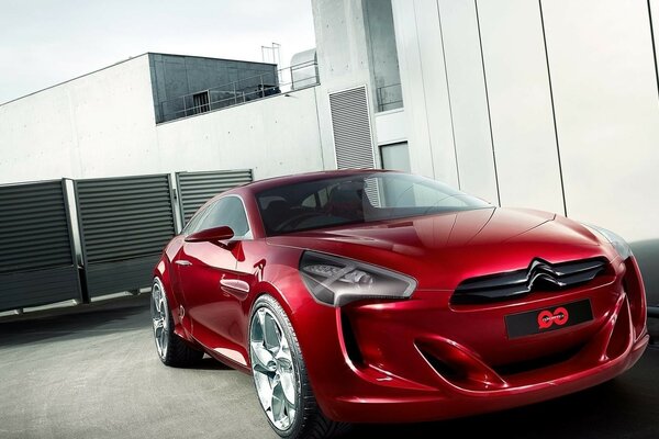 A bright scarlet car polished to a shine against a background of gray concrete