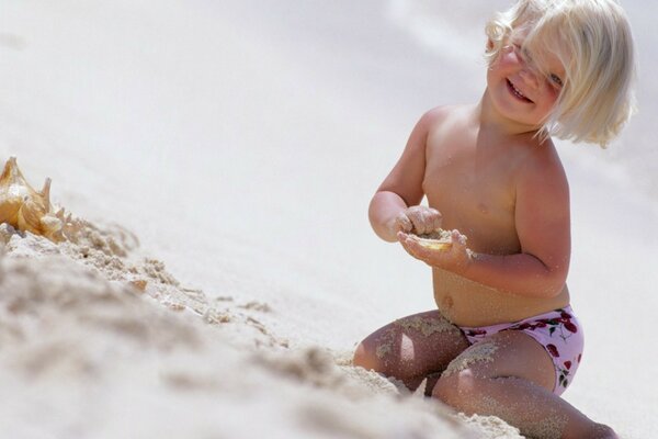 The child is sitting on the snow-white sand