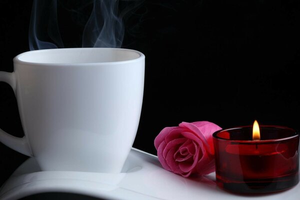 Mug, rose and candle on black background