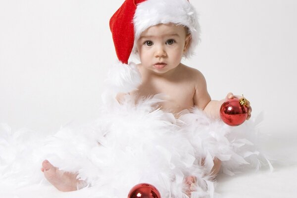 Enfant dans un bonnet de Noël, dans les plumes et avec une boule de Noël