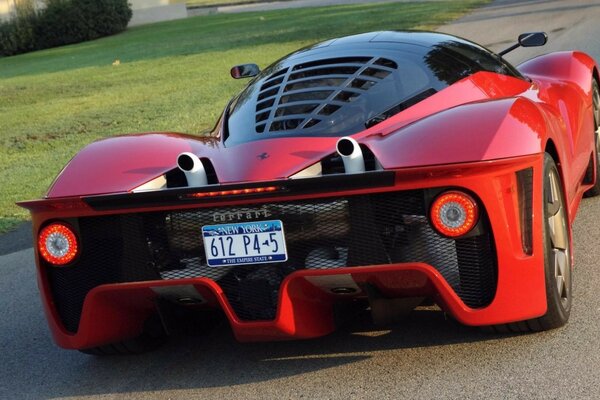 A red sports car on an asphalt road next to a green lawn