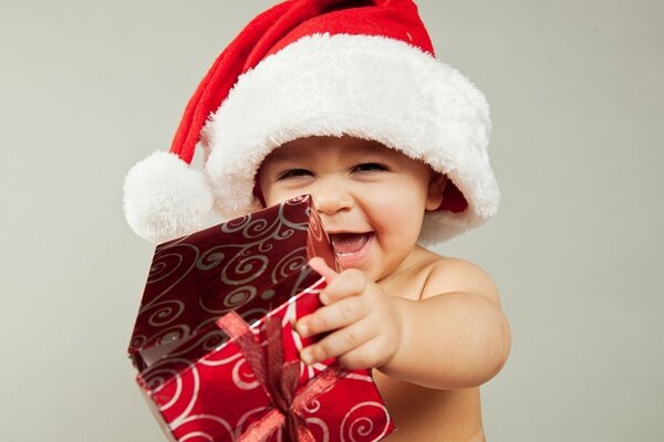 Baby in einer Weihnachtsmütze mit einem Geschenk