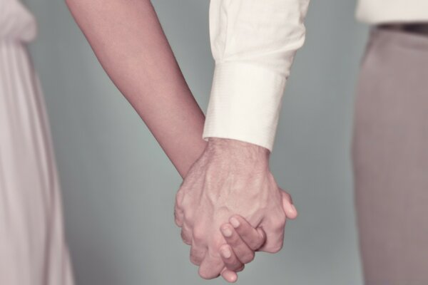 A man and a woman in light outfits holding hands tightly