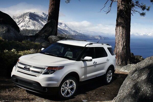 Ford SUV blanc parmi la forêt sur fond de montagnes