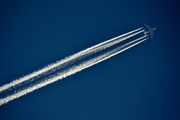 Un aereo in un cielo blu brillante vola e lascia due tracce bianche