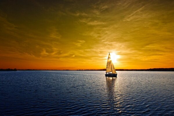 A sailboat walks on the water surface at sunset