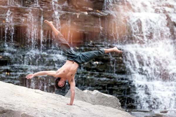 Un uomo esegue una posizione su una mano vicino a una cascata