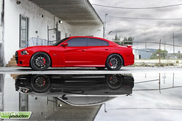 A red car is reflected in a puddle of black and white