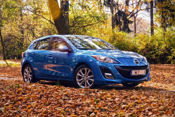 Nuevo coche azul Mazda en el bosque de otoño