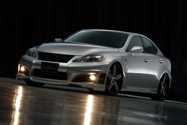 A gray car on a dark background with its headlights on