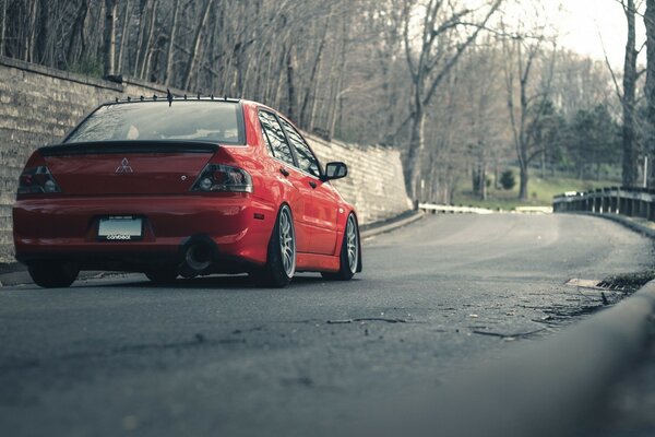 A red car is driving on the road to the forest