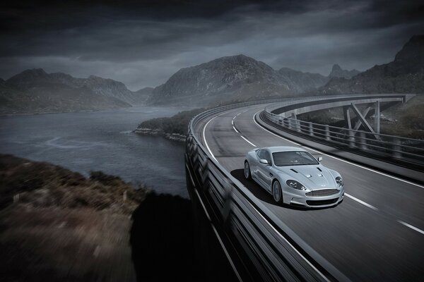 A silver car rushes across the bridge