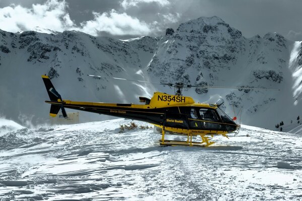 Elicottero giallo-nero sulla neve sullo sfondo delle montagne