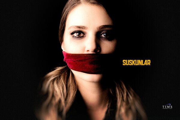 A woman with a blindfold over her mouth on a dark background