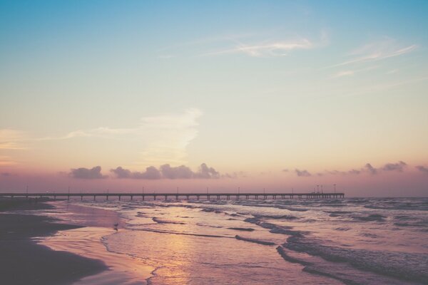 Un puente en la distancia y las olas en el fondo de un cielo rosa y azul