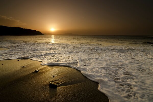 Sea foam on the sandy shore and sunset