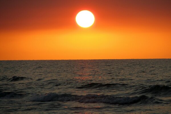 Sur la mer, le soleil se couche sur fond rouge-orange