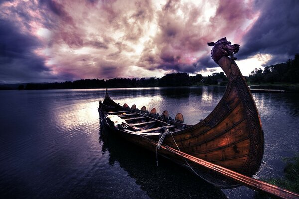 A boat similar to a Viking drakkar is moored on the lake at sunset