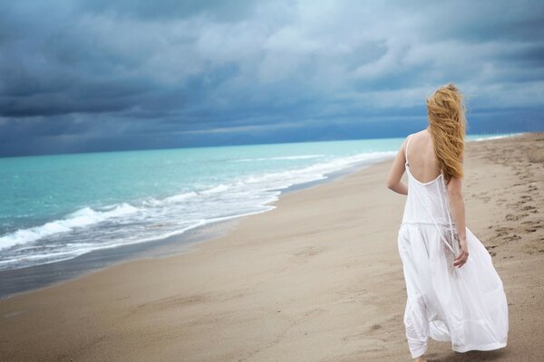 Hermosa chica en vestido blanco camina por la playa