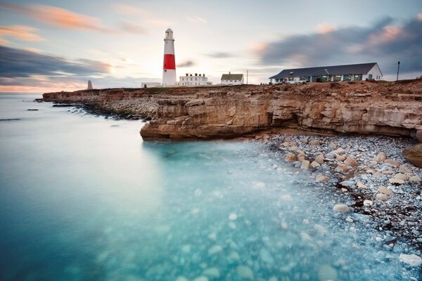 The ocean washes a rocky beach, a lighthouse is visible in the distance