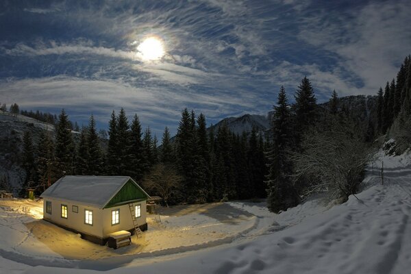 Winter evening, windows are lit in a wooden house