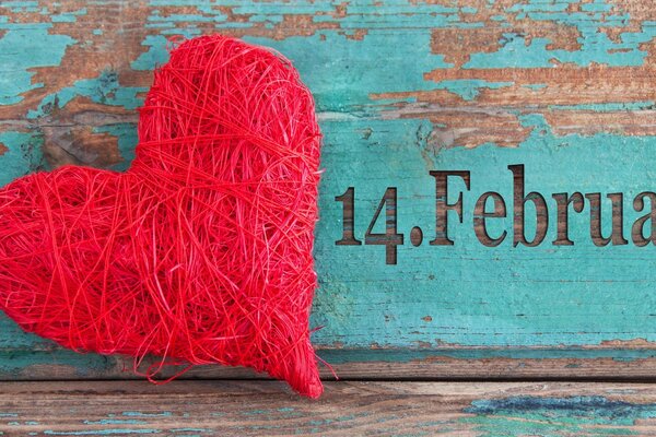 A red heart made of thread against a peeling board painted with blue paint on February 14