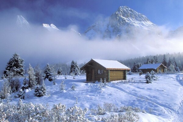 Cabaña en el bosque de invierno en el fondo de las montañas