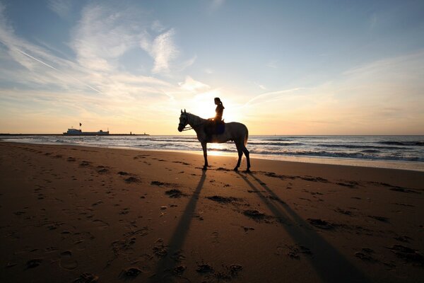 Mädchen auf einem Pferd am Strand am Meer bei Sonnenuntergang