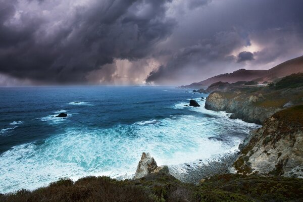 Deniz suyu, bulutlu gökyüzünün altındaki kayalık kıyılarda öfkeleniyor