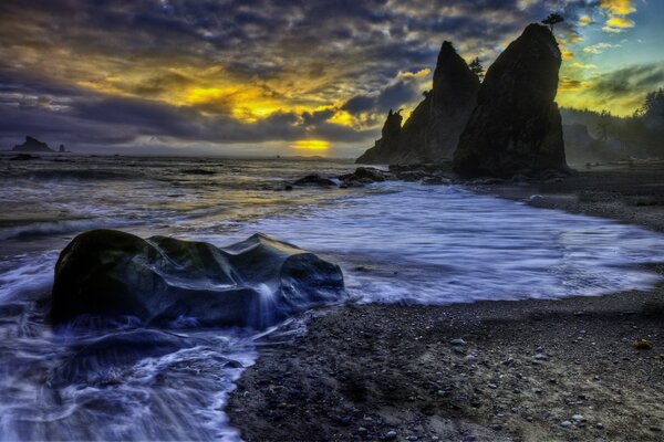 Olas en la costa rocosa al atardecer con cielos nublados