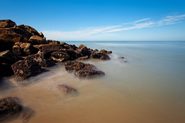 Calm sea water at the rocky shore under the blue sky