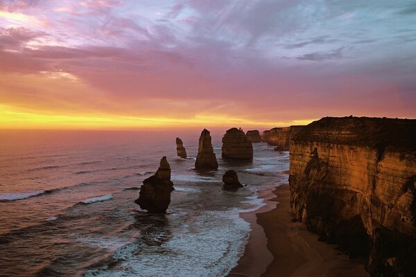 Pedras em pé no mar no fundo do pôr do sol