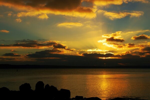 Ein wunderschöner Sonnenuntergang über dem ruhigen Meer, die Strahlen der untergehenden Sonne haben die Wasseroberfläche und die Wolken golden gefärbt